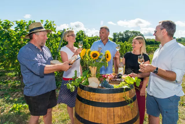 Fünf Personen stehen in den Reben um ein altes Weinfass