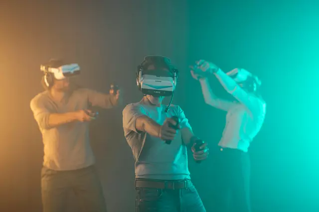 Drei Menschen in einem Raum mit VR-Brillen und Spielekosolen